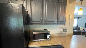 Una cocina con armarios oscuros, un refrigerador negro, un microondas y piso de baldosas.
