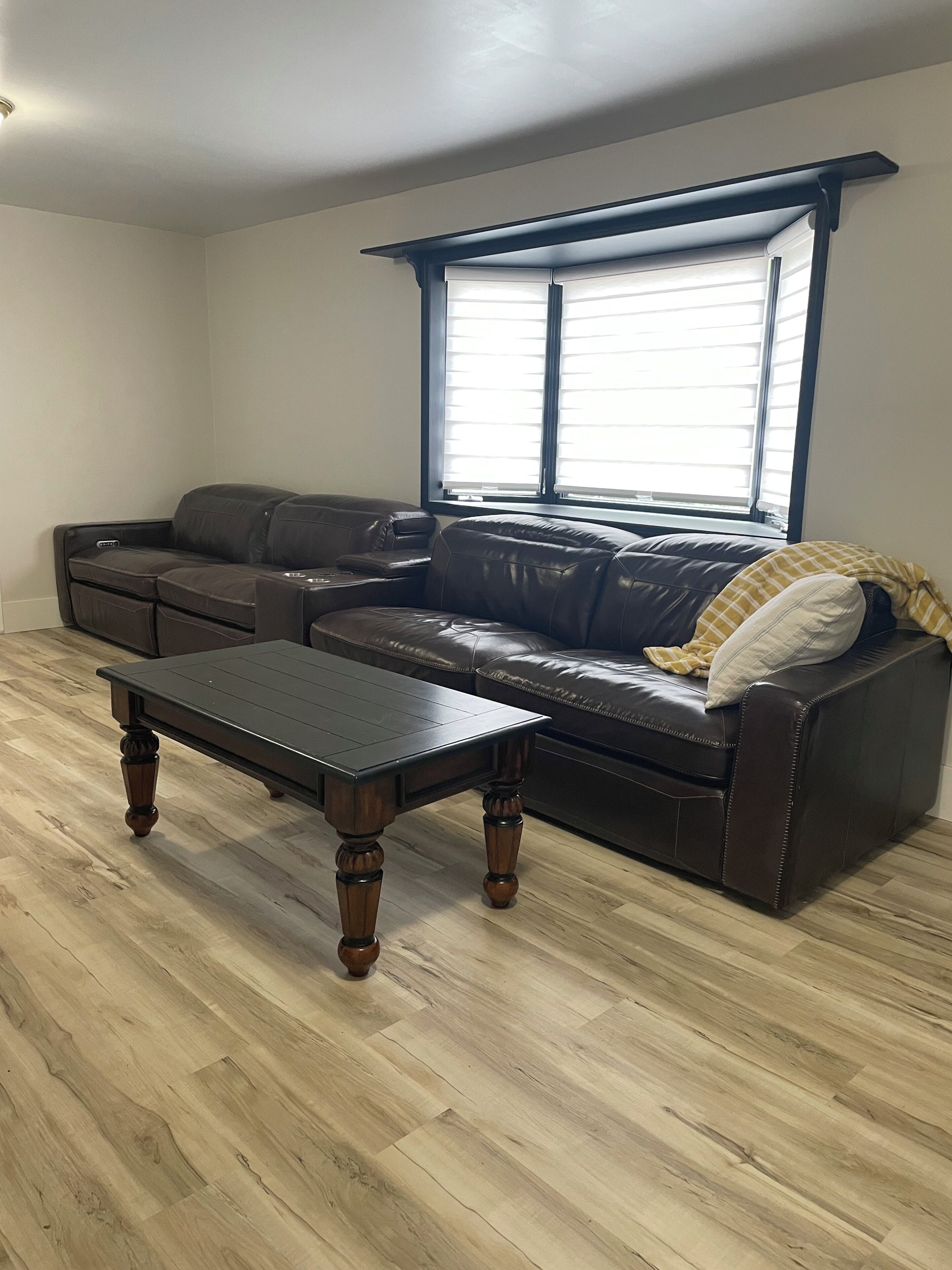 Una sala de estar con un sofá de cuero, una mesa de centro de madera y un ventanal con persianas.