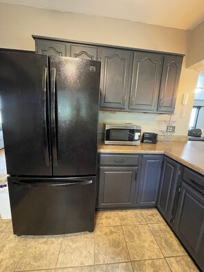 A kitchen with dark cabinets, a black refrigerator, a microwave, and a dishwasher.