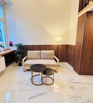 A modern living room with a sofa, two round tables, a lamp, and a potted plant. - Premium Heritage Loft on Piotrkowska (Łódź)