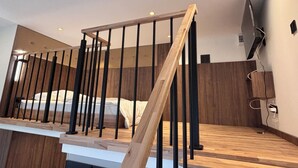 A modern bedroom with a wooden staircase, a bed, and a TV mounted on the wall. - Premium Heritage Loft on Piotrkowska (Łódź)