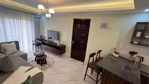 Een moderne woonkamer met een bank, salontafel, televisie en een keukenhoek met een aanrecht en stoelen.