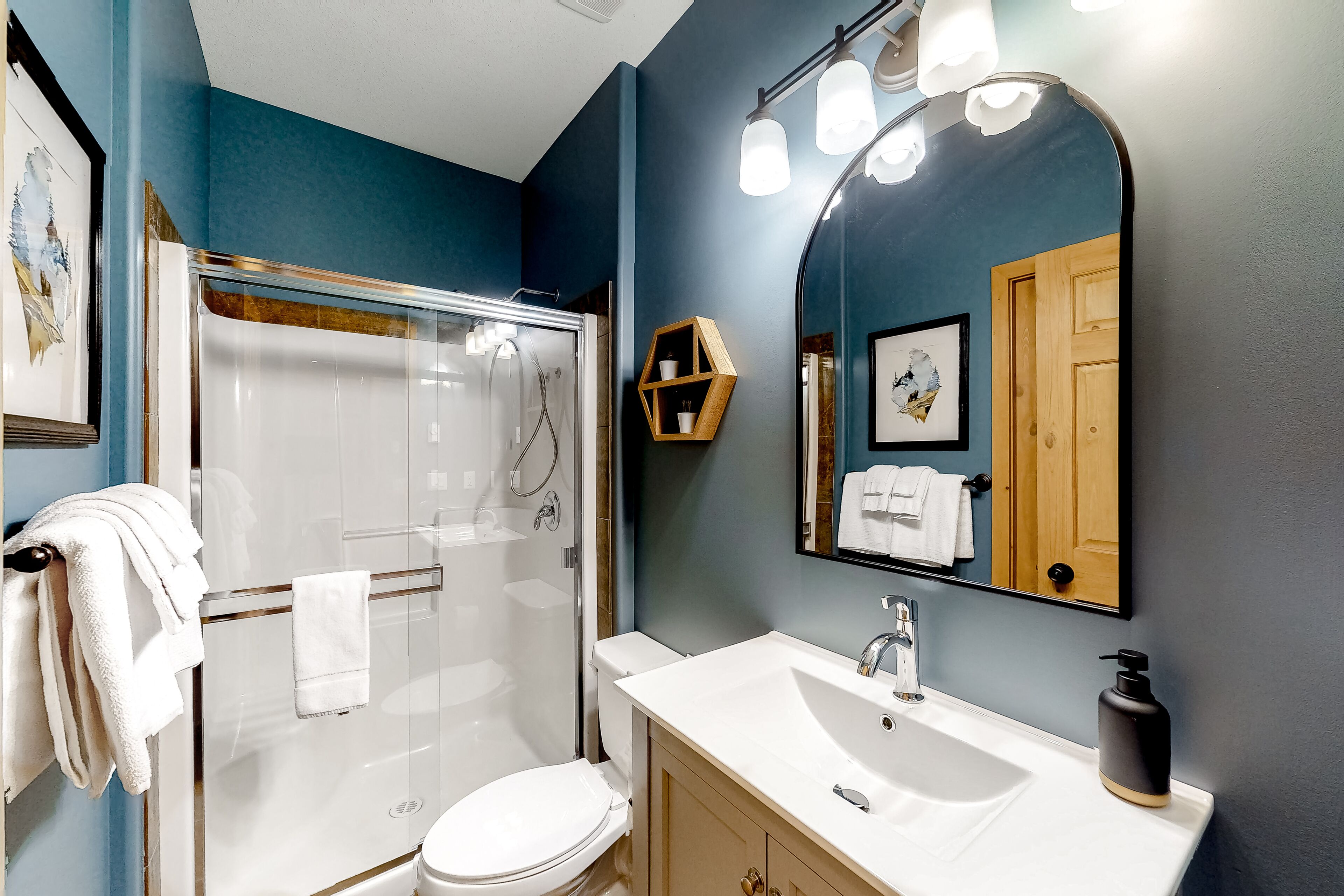 A modern bathroom with a glass shower enclosure, a white sink, and a large mirror.