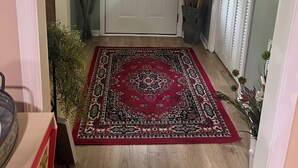A hallway with a wooden floor, a red patterned rug, a white door with a glass window, and a white wall with a 'welcome' sign. - 3/2 house in Statesboro with nearby GA Southern and Savannah (Statesboro)
