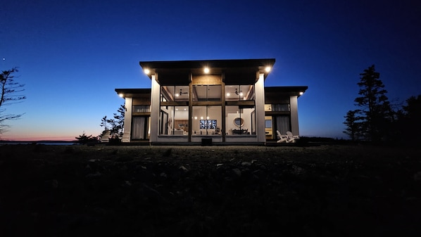 Une maison moderne avec une façade en verre, un balcon et une vue sur l’océan.