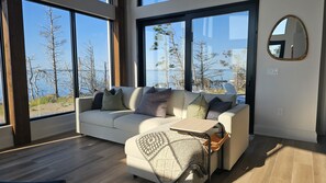 A modern living room with a sofa, a coffee table, and a view of trees and water.