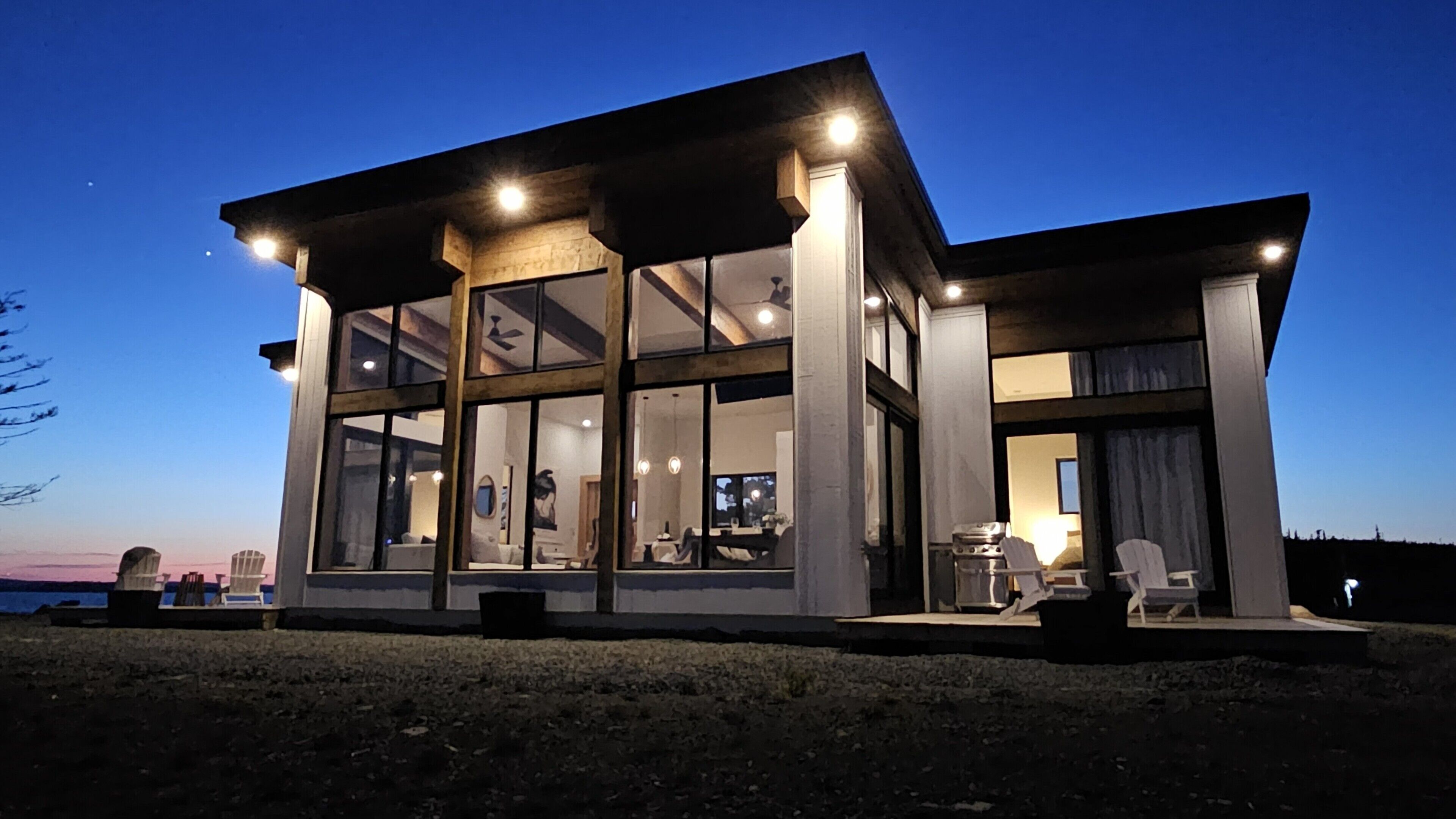 Une maison moderne dotée de grandes baies vitrées, d’un coin repas et d’une cuisine visible de l’intérieur.