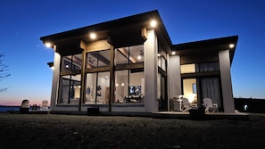 Une maison moderne dotée de grandes baies vitrées, d’un coin repas et d’une cuisine visible de l’intérieur.