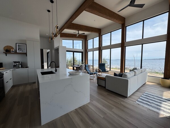 A modern kitchen with a large island, a dining area with a view, and a living space with a sofa and a rug.