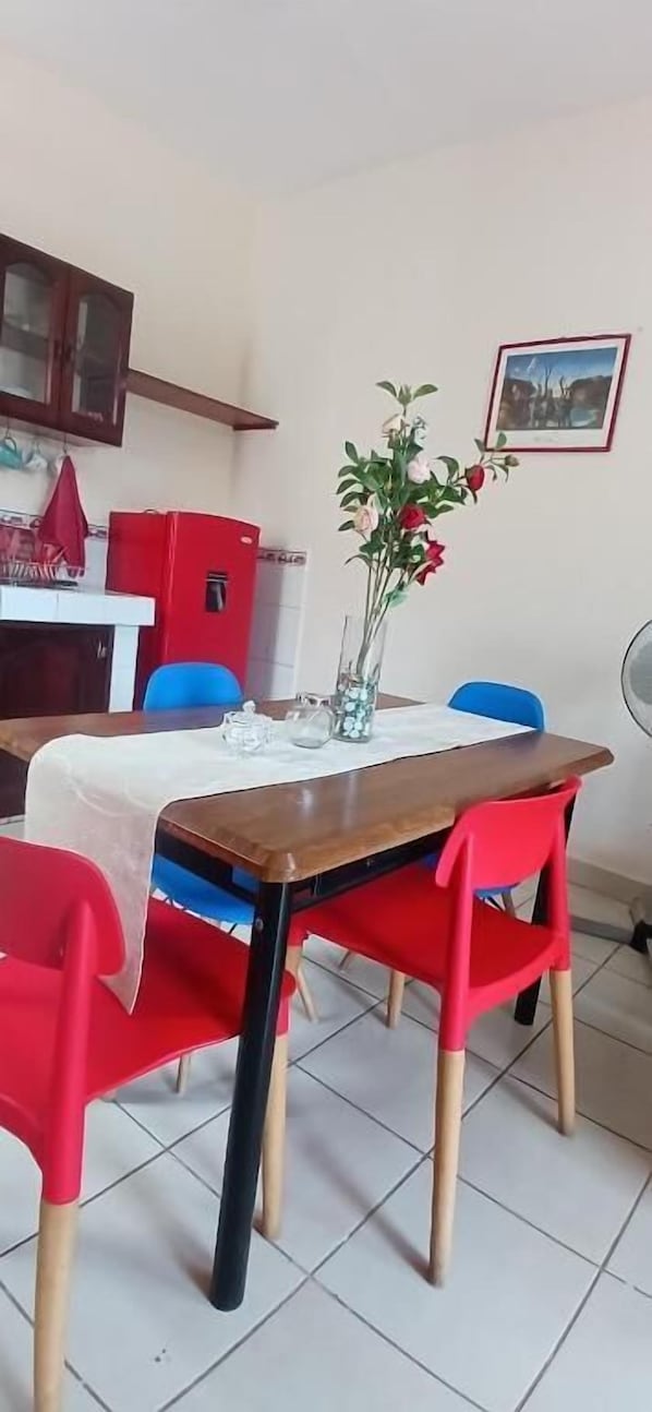 A dining area with a wooden table, red chairs, a vase with flowers, and a red refrigerator.