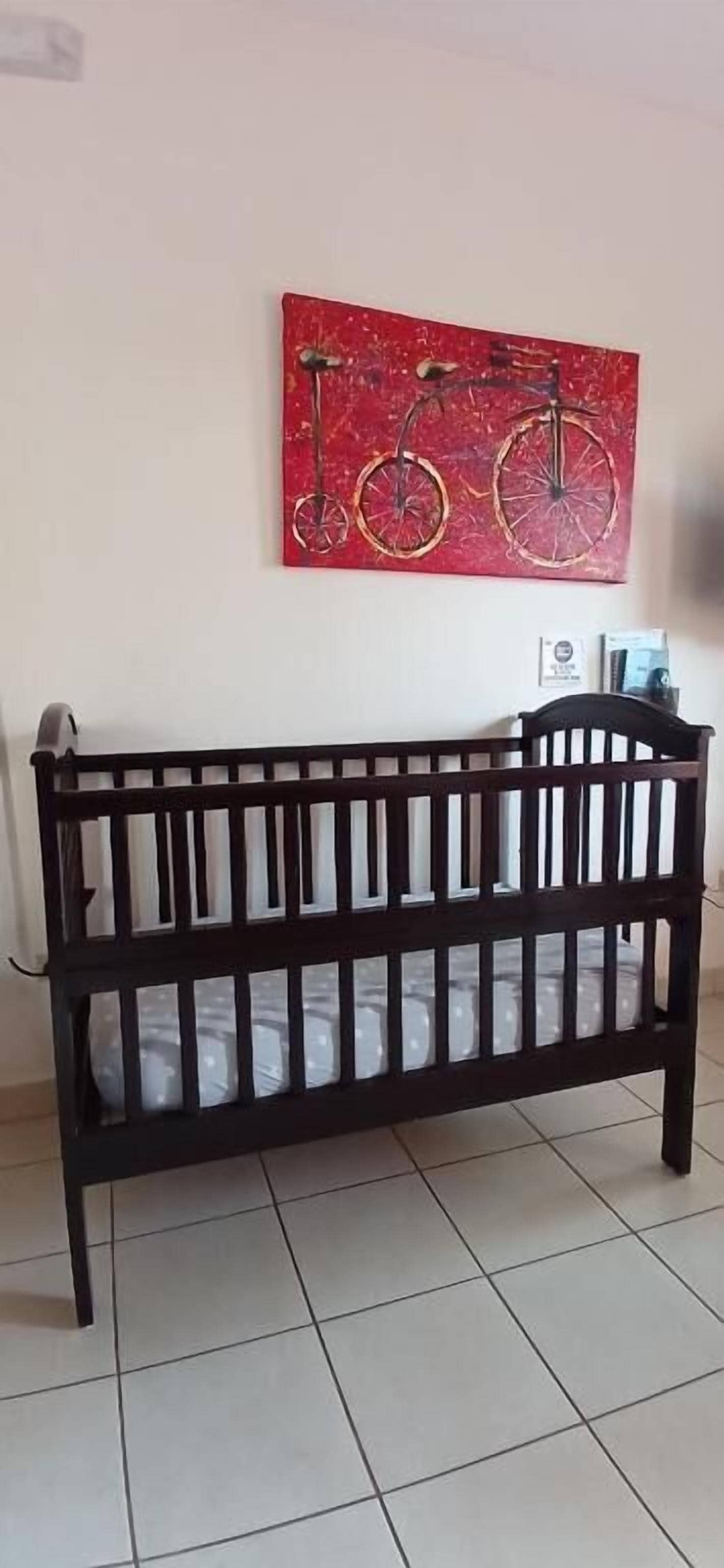 A crib in a room with a red wall and a painting of bicycles.