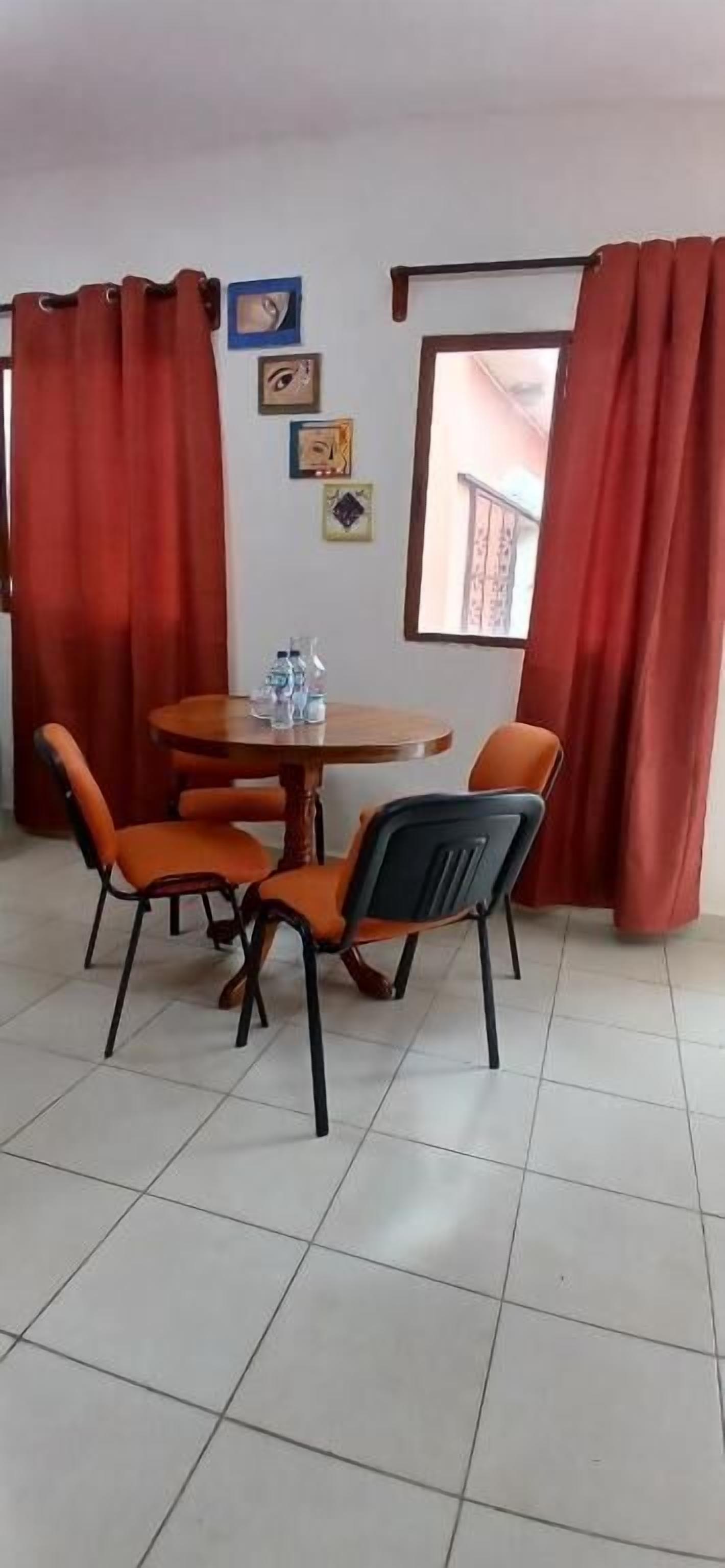 Un comedor con una mesa redonda y cuatro sillas, cortinas rojas y una ventana con vistas al balcón.