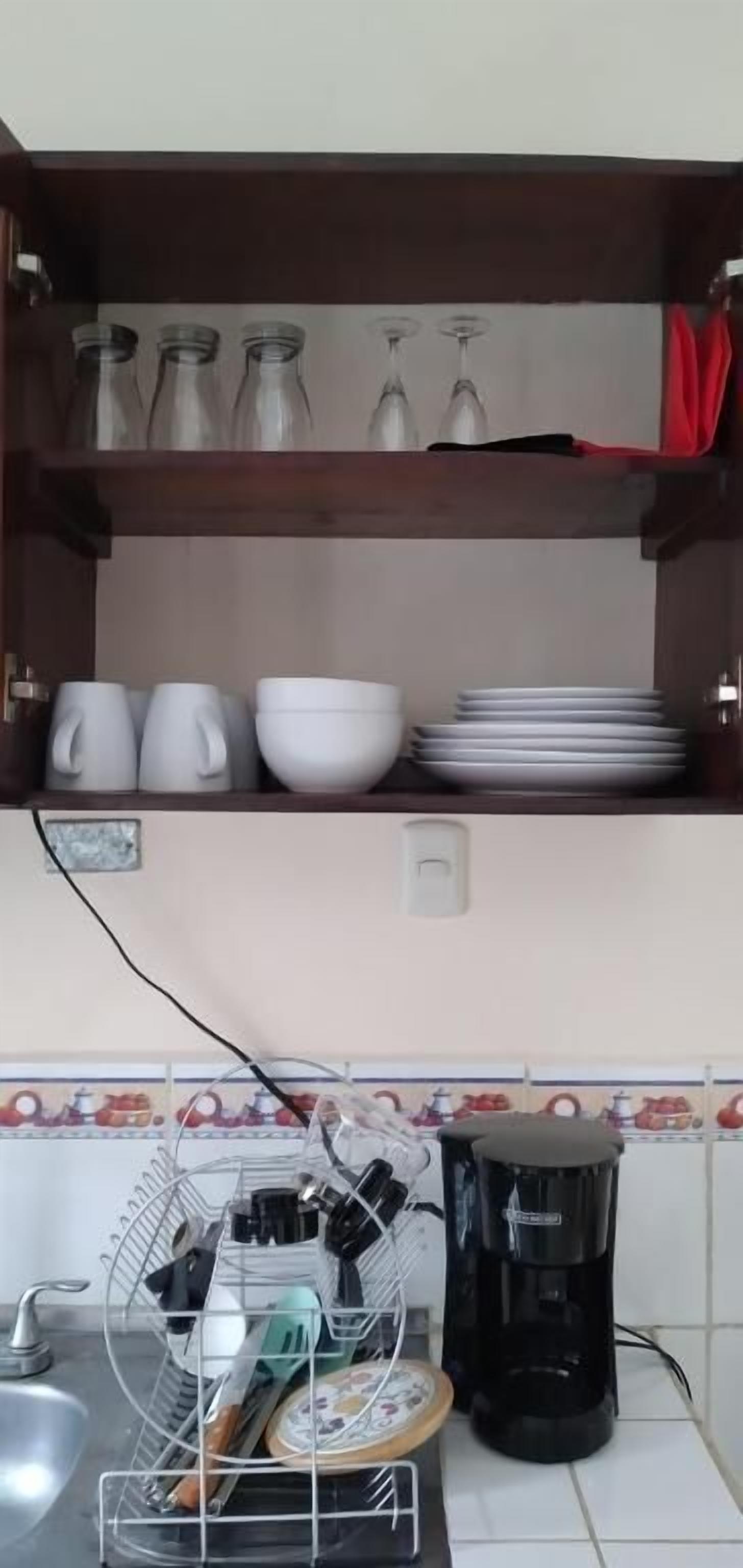 A kitchen with a shelf holding glassware and a coffee maker on the counter.