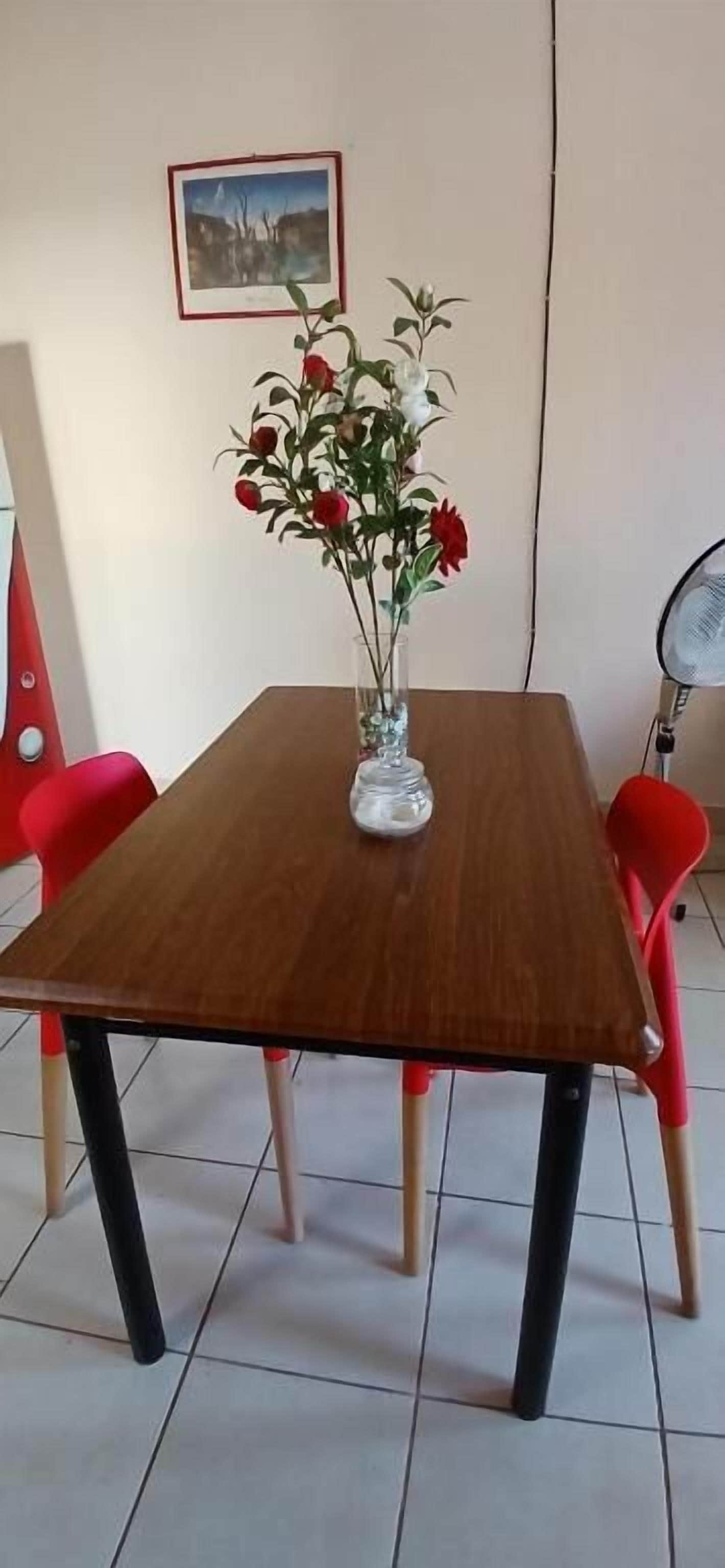 A dining table with a vase of flowers, red chairs, and a picture on the wall.