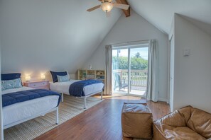 Ein Schlafzimmer mit zwei Betten, einem Deckenventilator, einem großen Fenster mit Vorhängen und einem Balkon.