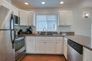 A modern kitchen with white cabinets, stainless steel appliances, a granite countertop, and a window with blinds.