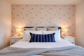 A neatly made bed with a patterned pillow, two bedside lamps, and a wall with a seagull print.