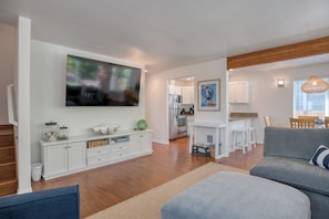 Ein modernes Wohnzimmer mit Flachbildfernseher, einem grauen Sofa und einer Küche im Hintergrund.
