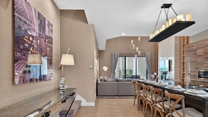 Ein modernes Wohnzimmer mit einer Couch, einem Essbereich mit Stühlen, einer Küche und einem großen Stadtbild an der Wand.