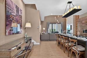 A modern living room with a sofa, dining area with chairs, a kitchen with a TV, and a large cityscape painting on the wall. - Spacious 3BR/3.5BA Home Near Disney in Kissimmee (Kissimmee)