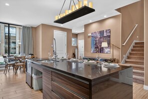 A modern kitchen with a central island, a dining area with wooden chairs, and a staircase leading to an upper level. - Spacious 3BR/3.5BA Home Near Disney in Kissimmee (Kissimmee)