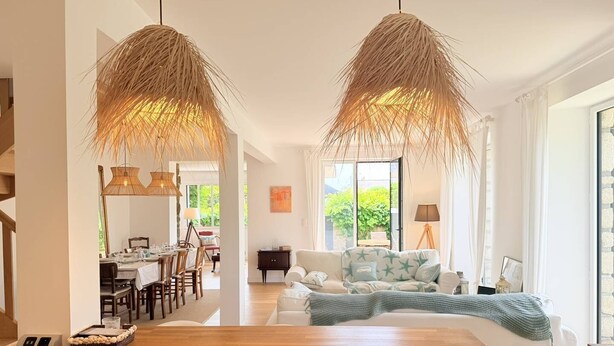 Ein modernes Wohnzimmer mit einem Holzesstisch, einer Couch mit sternförmigen Kissen und zwei hängenden Korbstühlen.