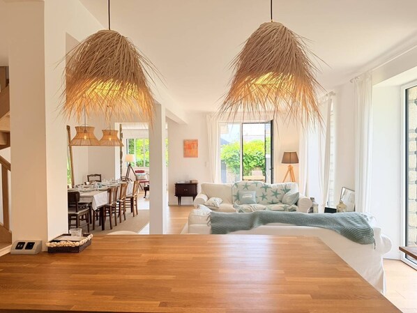 A modern living room with a wooden dining table, a sofa with star-patterned cushions, and two hanging wicker lamps. - Spacieuse maison 8px, proche plage et centre-ville (QUIBERON)