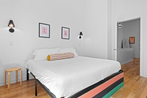 Een slaapkamer met een bed, een klein krukje en wandlampen.