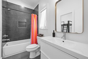 Een moderne badkamer met een badkuip, toilet en een wastafel met spiegel.