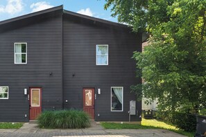 Een gebouw met twee verdiepingen, een donkere gevel, twee zichtbare ramen en een rode deur.