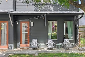 Ein Haus mit dunkler Fassade, einer Veranda mit zwei Stühlen und einem Tisch sowie einem Fenster mit Vorhängen.