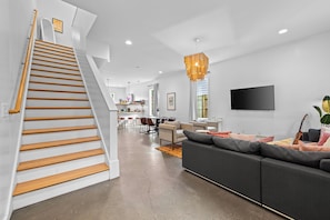 Ein modernes Interieur mit Treppe, einem Wohnbereich mit Sofa, einem Essbereich und einem an der Wand montierten Fernseher.