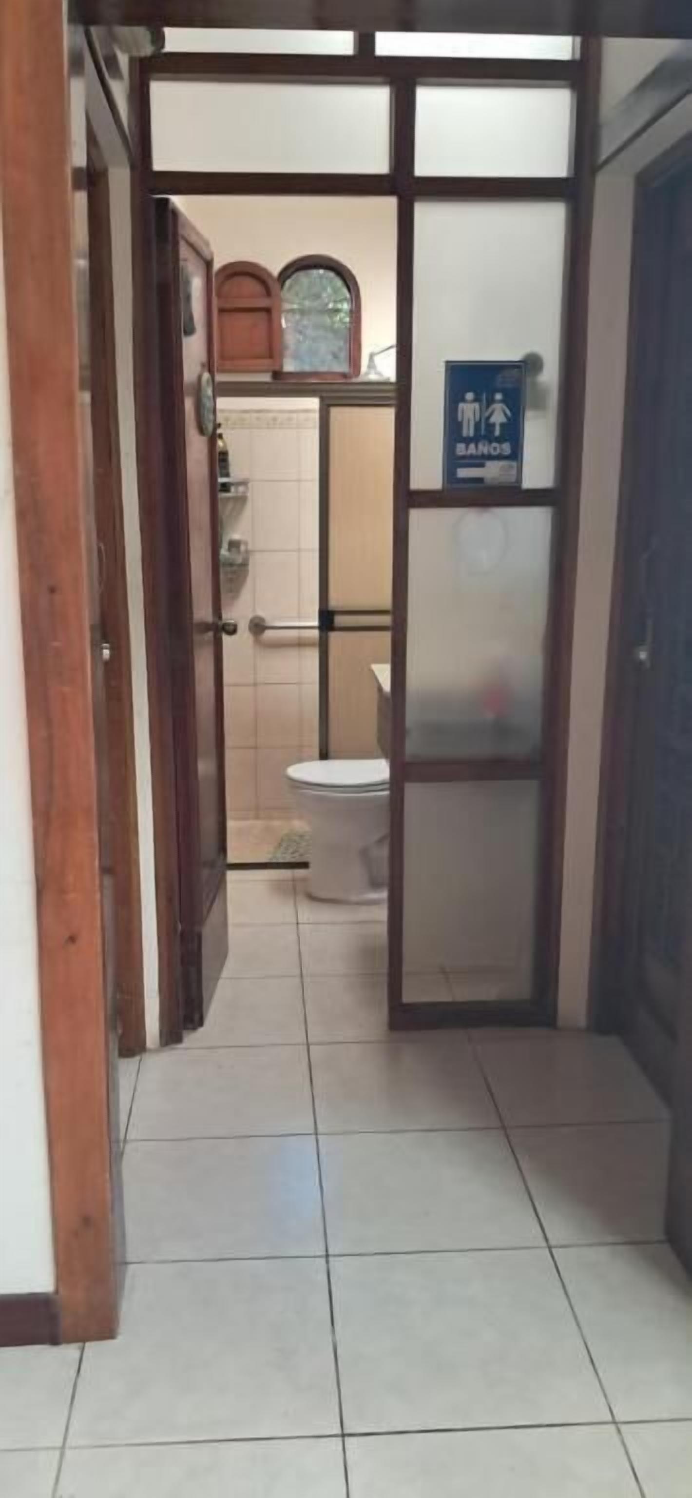 Passadís estret que condueix a un bany amb vàter, rentapèns i zona de dutxa.