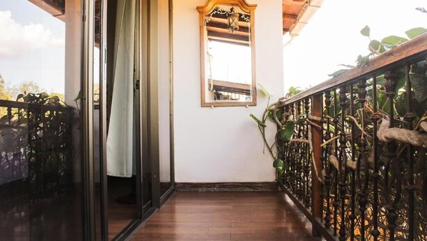 Un pasillo con suelo de madera, una puerta de cristal, barandilla de metal con plantas y un espejo adosado a la pared.