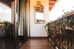 Un pasillo con suelo de madera, una puerta de cristal, barandilla de metal con plantas y un espejo adosado a la pared.