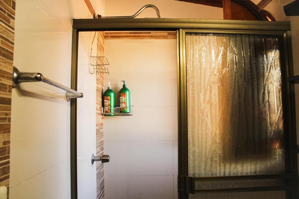 A bathroom with a shower, a towel rack, and two green bottles on a shelf.