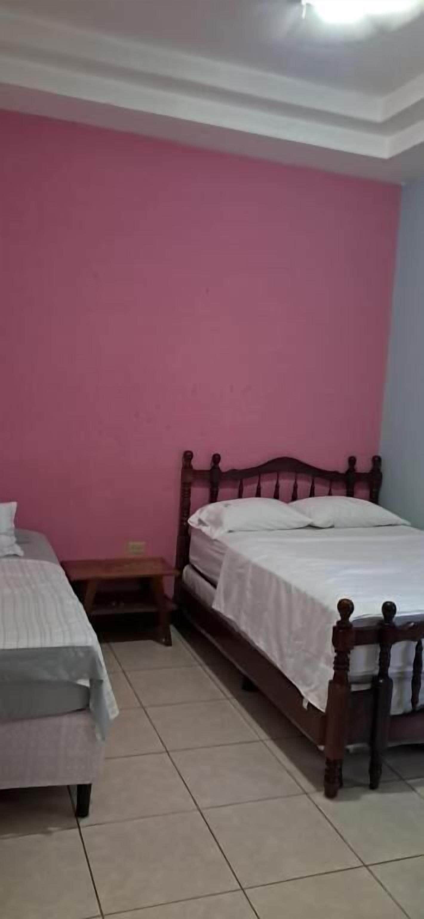 Un dormitorio con dos camas, una pared rosa y un cabecero de madera.
