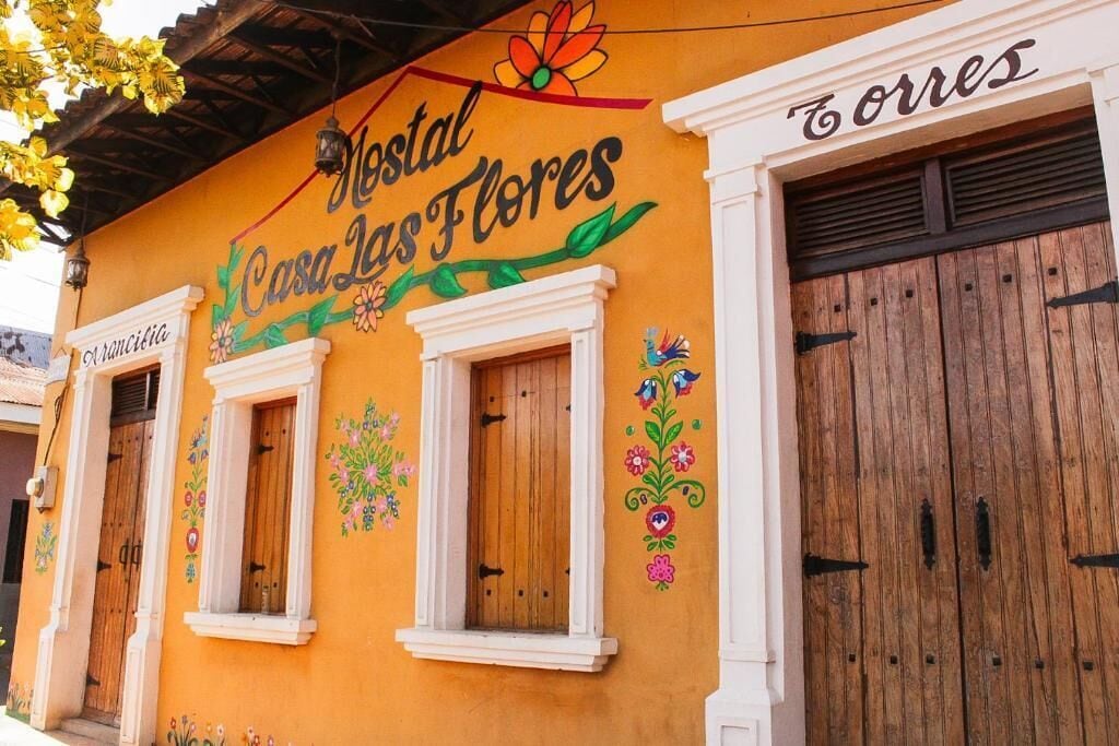 Um edifício com uma placa indicando 'Mestal Casa las Flores' e uma porta de madeira com a inscrição 'Torres'.