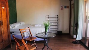 Una habitación con una cama, una silla de madera, una mesita redonda con una planta y un tendedero.