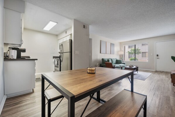 A modern kitchen with a wooden table and bench, a refrigerator, and a dining area with a sofa and coffee table.