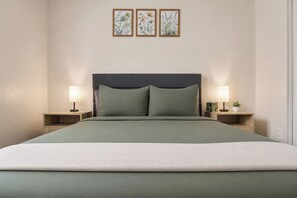 A bed with a dark headboard, two bedside tables with lamps, and three framed botanical prints on the wall.