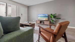 Una sala de estar con un sofá, un sillón de cuero, una mesa de centro, un televisor y una planta.
