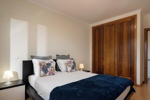 Quarto com cama, mesas de cabeceira, guarda-roupa de madeira e abajur.