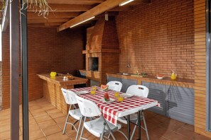 Cozinha externa com parede de tijolos, teto de madeira e mesa posta com cadeiras.