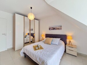 Ein Schlafzimmer mit Bett, Nachttischen, einem Spiegel und einer Pendelleuchte.