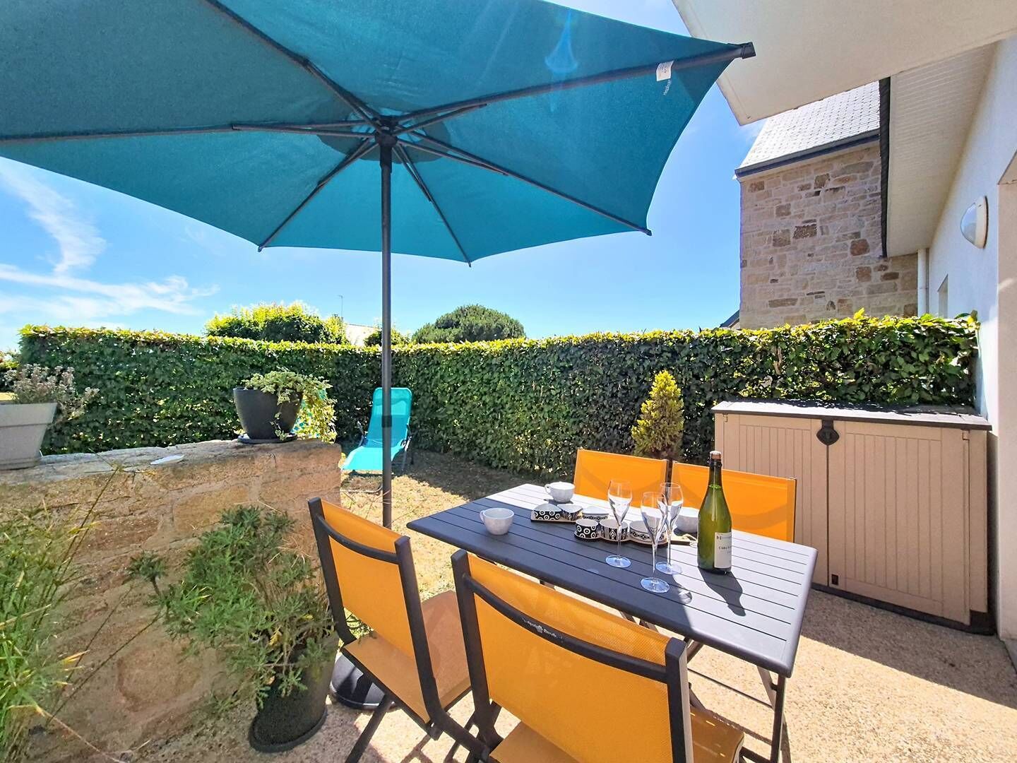 Eine Terrasse mit Tisch, Stühlen, Sonnenschirm und einer Weinflasche.