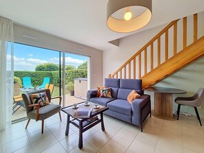 Ein modernes Wohnzimmer mit einer Couch, einem Couchtisch und einem Essbereich mit Stühlen. Eine Treppe führt zu einer oberen Ebene.