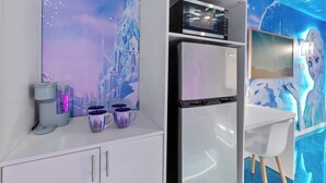 Una cocina moderna con refrigerador, microondas y cafetera, y un mural en la pared que muestra un paisaje invernal.