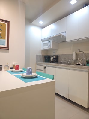 Een moderne keuken met witte kasten, een magnetron, een koffiezetapparaat en een spoelbak.