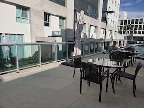 Een terras op het dak met glazen hekwerk, buitenmeubilair en een zwembad.
